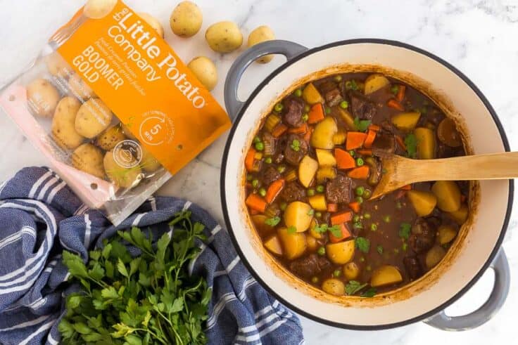 This classic Beef Stew is recipe is rich, flavorful and comes together in one pot! With tender chunks of beef and plenty of vegetables, it's healthy and comforting. #stew #beef #recipes #dinner overhead image of pot of beef stew with bag of little potatoes