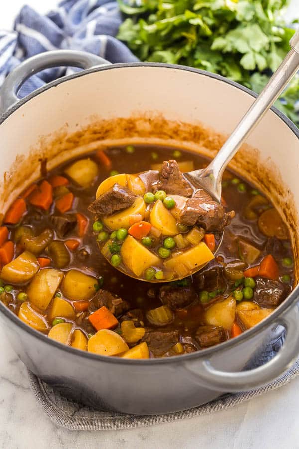 classic beef stew being ladled out of large pot