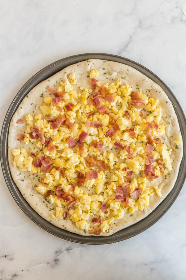 uncooked breakfast pizza with scrambled eggs and bacon