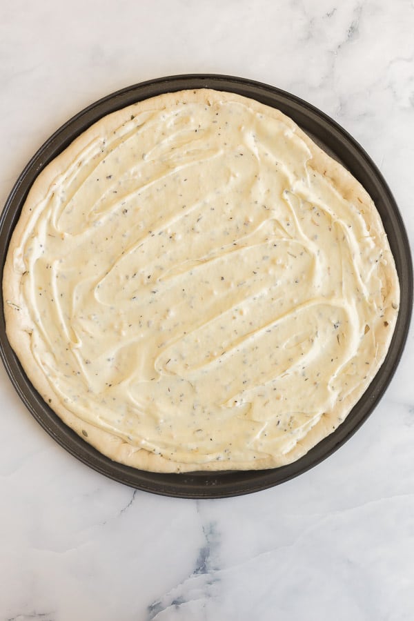 alfredo sauce spread on pizza dough in pizza pan