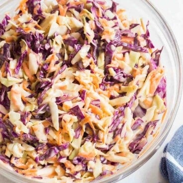 homemade coleslaw recipe in a glass bowl with blue towel on the side.