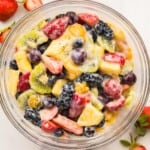 square image of creamy fruit salad in a glass bowl on marble.
