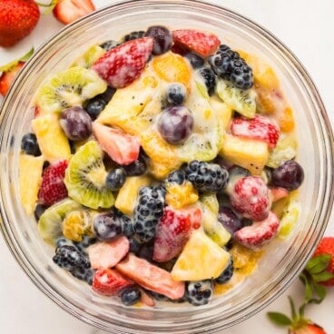 square image of creamy fruit salad in a glass bowl on marble.