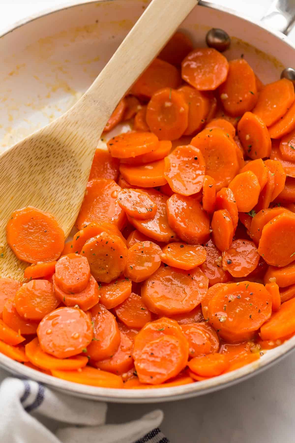 close up image of glazed carrots in a white skillet with a wooden spoon.