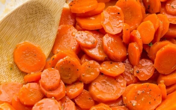 square image of glazed carrots in a white skillet with a wooden spoon.