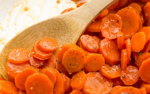 close up of glazed carrots in pan with wooden spoon