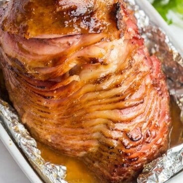 honey baked ham in white baking dish with foil around.