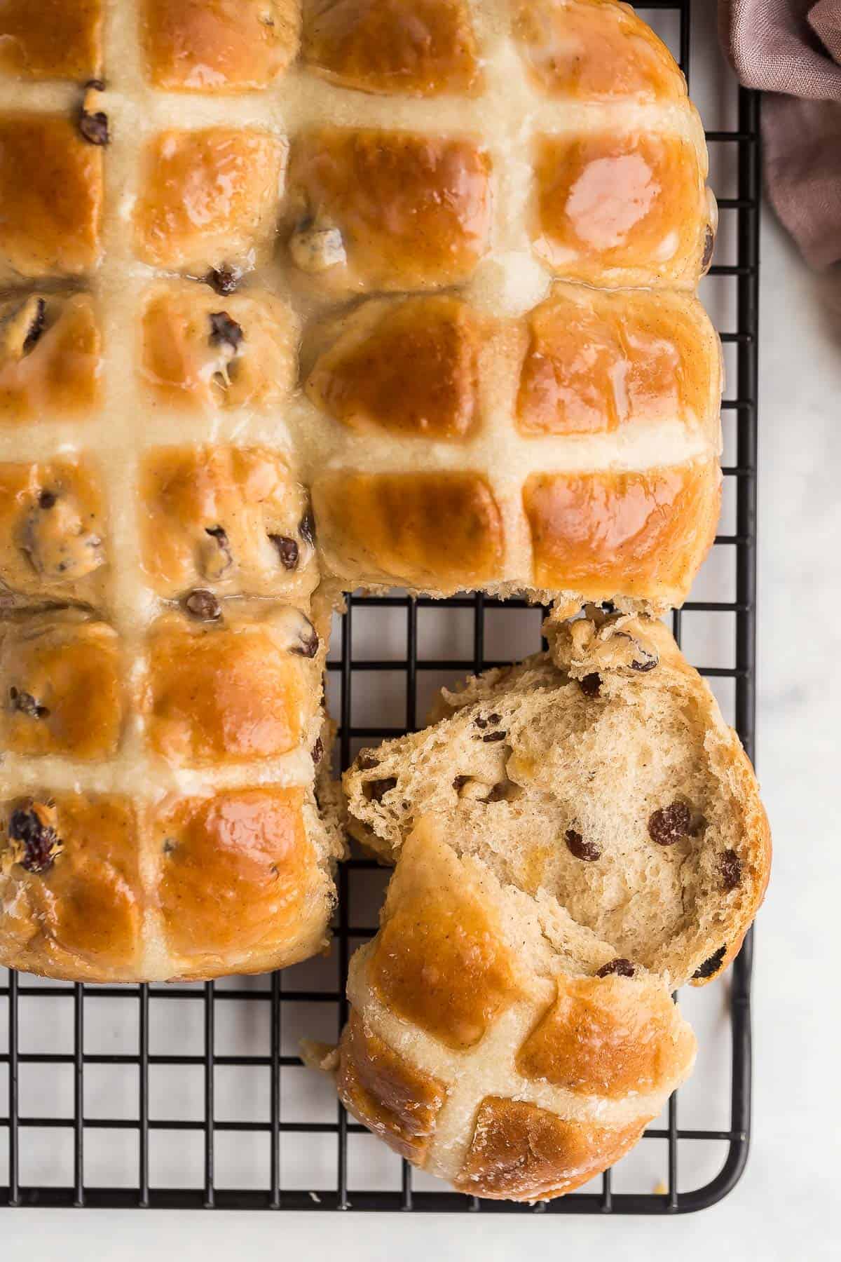 These Hot Cross Buns are sweet, fluffy, lightly spiced buns filled with raisins and marked with a white cross. They are traditionally served at Easter but delicious any time of year! #easter #baking #buns #recipes | easter recipes | easter baking | easter breakfast || easter brunch | cinnamon buns | cinnamon raisin buns | brunch recipes overhead image of hot cross buns on a cooling rack.
