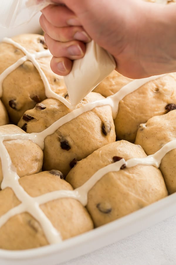 These Hot Cross Buns are sweet, fluffy, lightly spiced buns filled with raisins and marked with a white cross. They are traditionally served at Easter but delicious any time of year! #easter #baking #buns #recipes piping the flour mixture on the hot cross buns