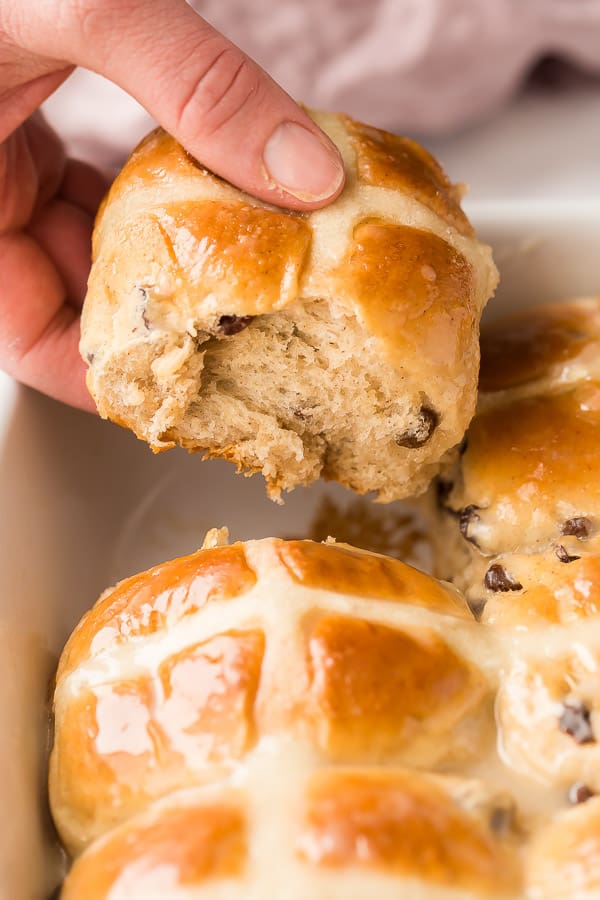These Hot Cross Buns are sweet, fluffy, lightly spiced buns filled with raisins and marked with a white cross. They are traditionally served at Easter but delicious any time of year! #easter #baking #buns #recipes hand pulling hot cross bun out of pan