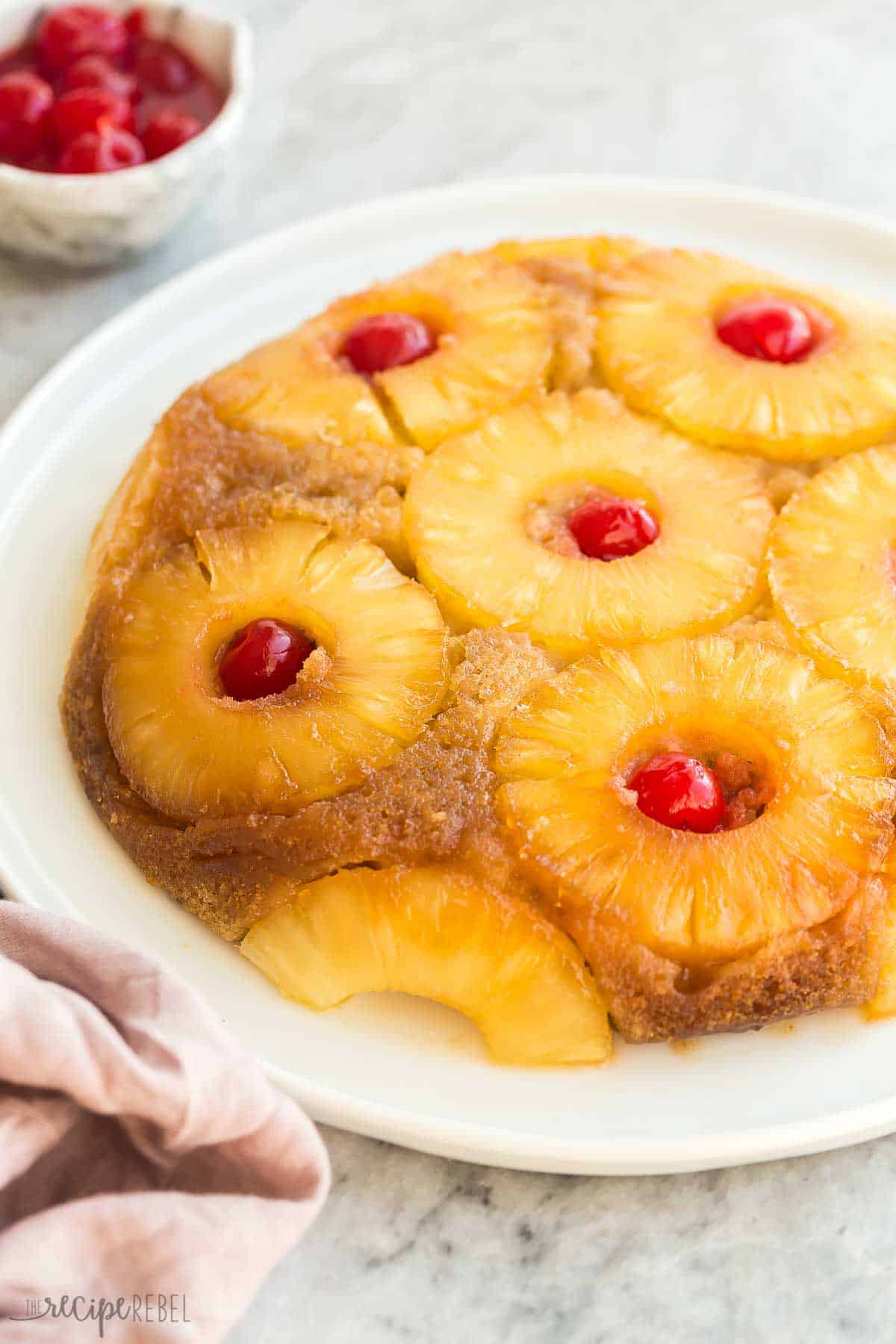 This easy Pineapple Upside Down Cake from scratch is a retro dessert made with one bowl and a whisk! It has brown sugar caramelized pineapple rings, a moist vanilla cake and maraschino cherries. #cake #dessert #recipe | dessert recipes | pineapple dessert | spring dessert | easter cake | easter dessert | fruit dessert | easy cake recipes | easy recipes pineapple upside down cake with cherries on a white plate.