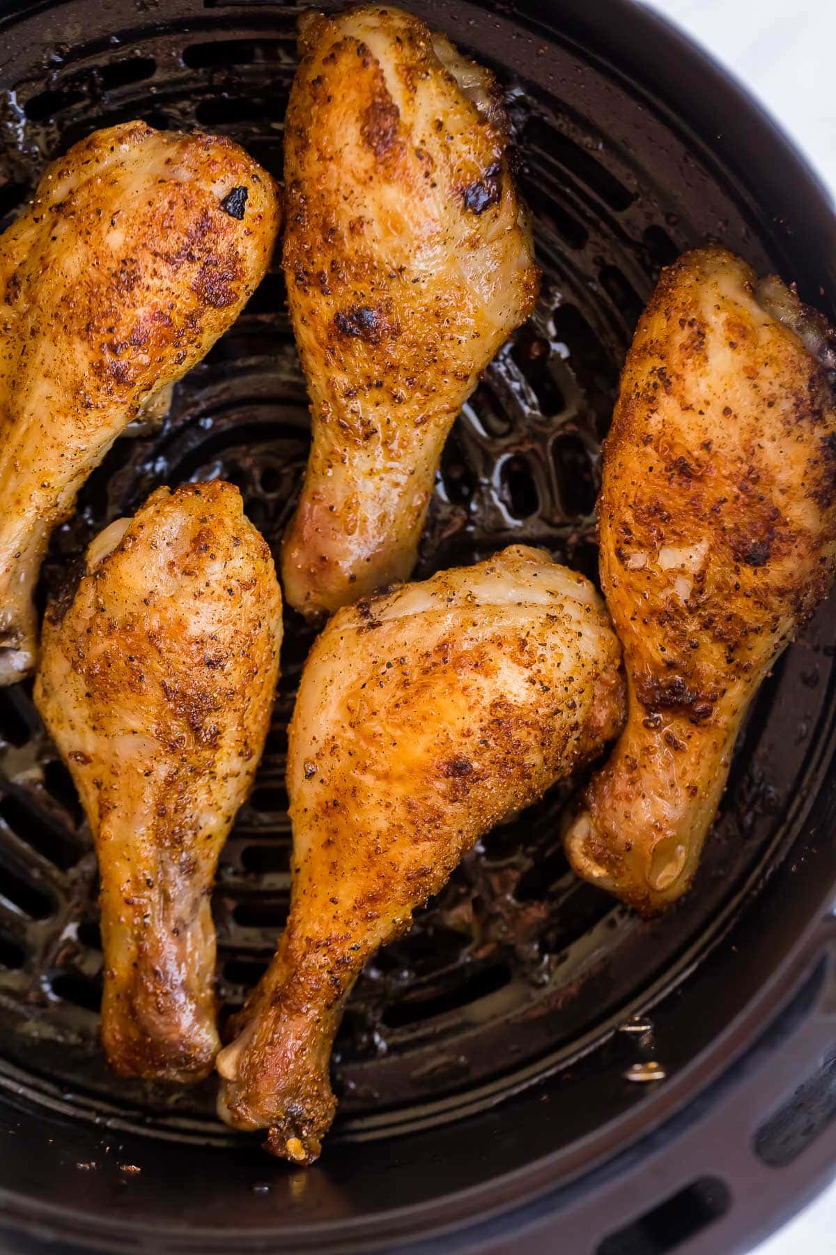 These Air Fryer Chicken Legs are tender, juicy and flavorful with a crispy exterior! The air fryer is the best and easiest way to cook those chicken drumsticks, with perfect results every time. #airfryer #chicken #recipes #dinner overhead image of air fryer chicken legs in air fryer basket.
