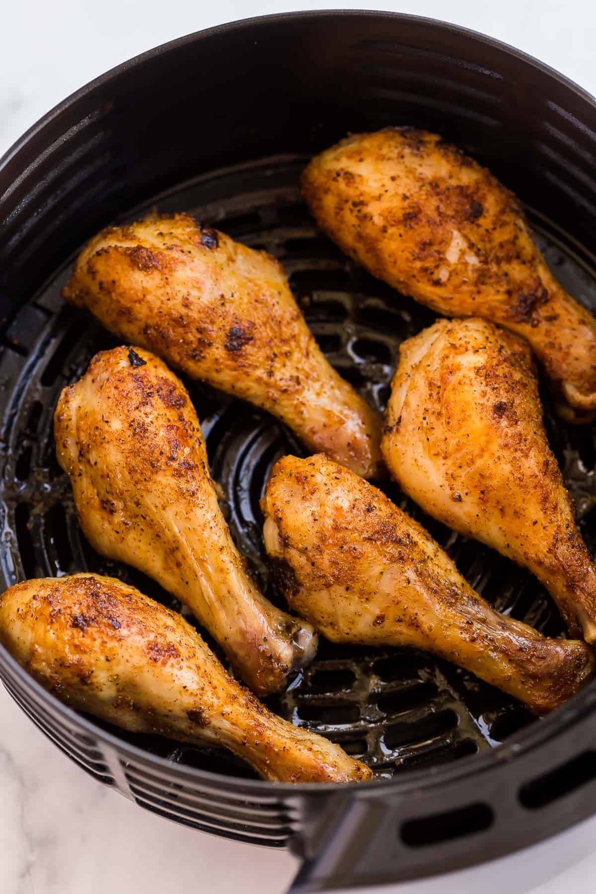 These Air Fryer Chicken Legs are tender, juicy and flavorful with a crispy exterior! The air fryer is the best and easiest way to cook those chicken drumsticks, with perfect results every time. #airfryer #chicken #recipes #dinner close up image of six chicken drumsticks in air fryer.