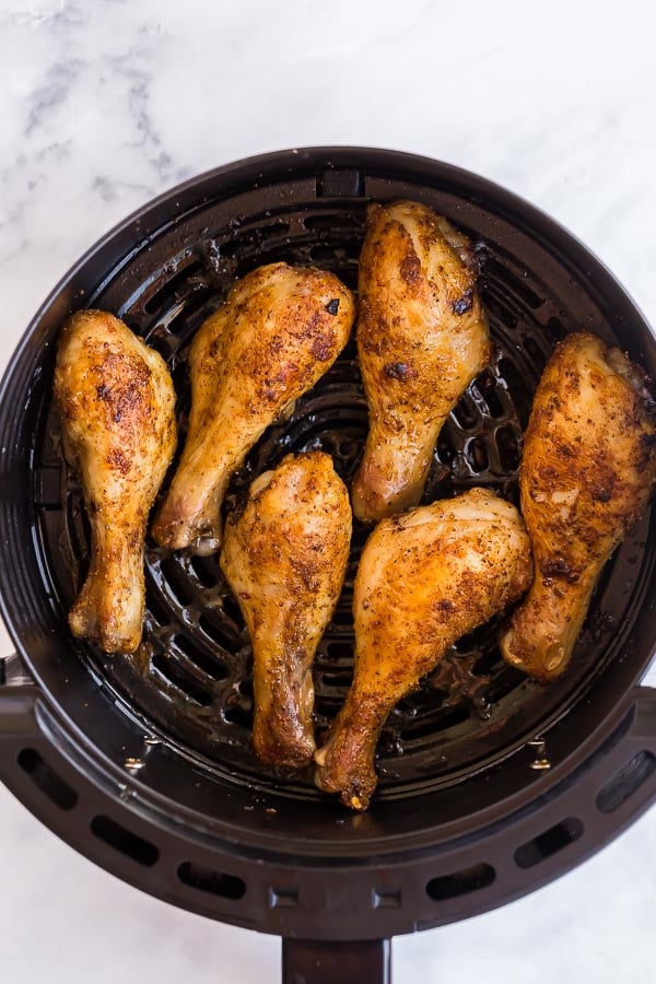 overhead image of cooked chicken drumsticks in air fryer basket