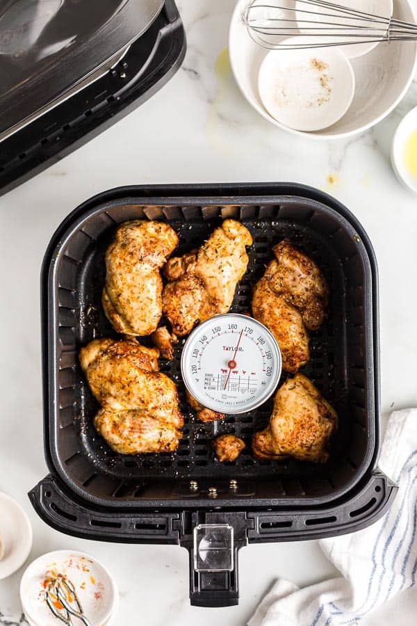 cooked chicken thighs in air fryer basket with thermometer at 165 degrees