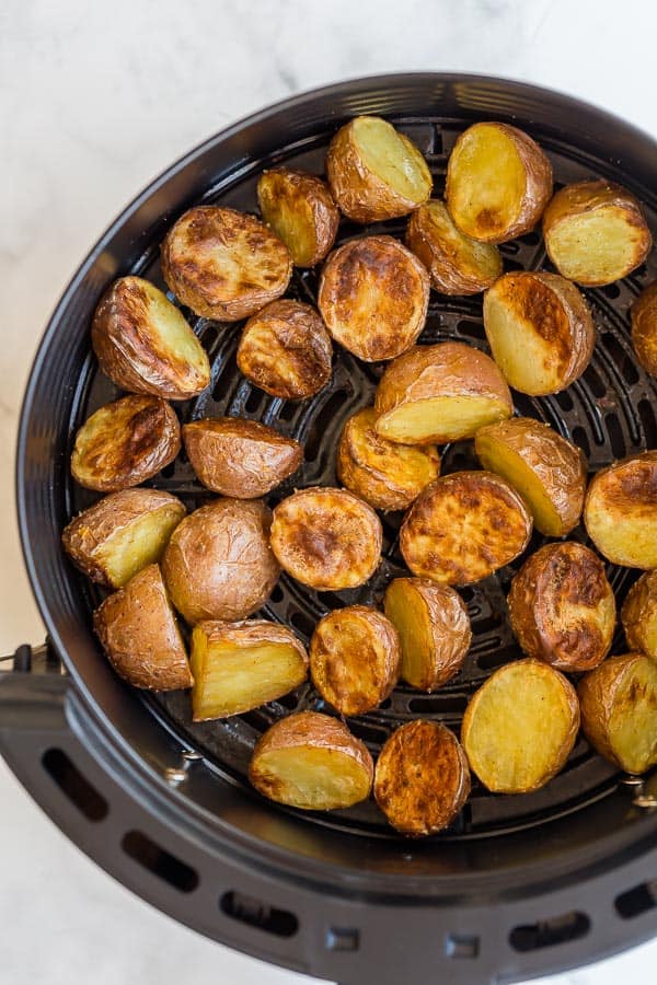 These crispy Air Fryer Potatoes are made with a few simple ingredients and little prep time! They are golden on the outside and fluffy on the inside. #airfryer #potatoes close up of cooked air fryer potatoes in basket