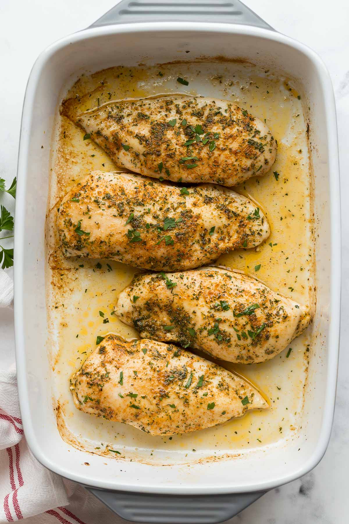 overhead image of four baked chicken breasts with fresh parsley.