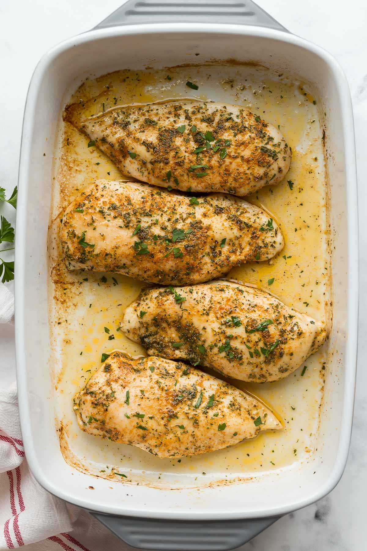 This Baked Chicken Breast comes out juicy and flavorful every time! With a simple spice rub and quick cook time, it's perfect for any night of the week! #chicken #dinner #recipes overhead image of four baked chicken breasts with fresh parsley.