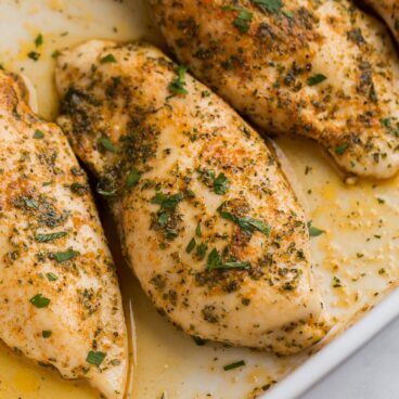 close up image of baked chicken breasts in baking dish with juices.