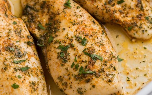 close up image of baked chicken breasts in baking dish with juices.