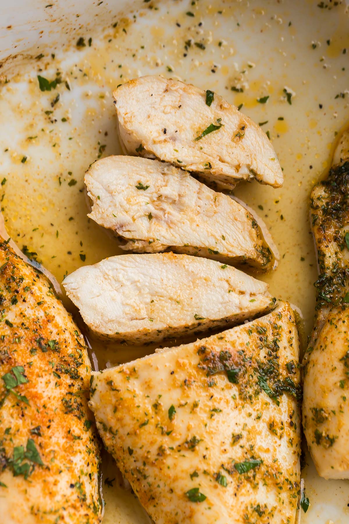 three slices of baked chicken breasts lying down in pan.