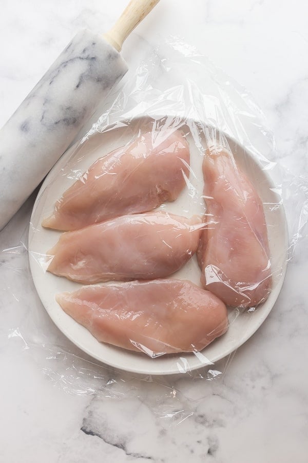 raw chicken breasts on plate under plastic wrap
