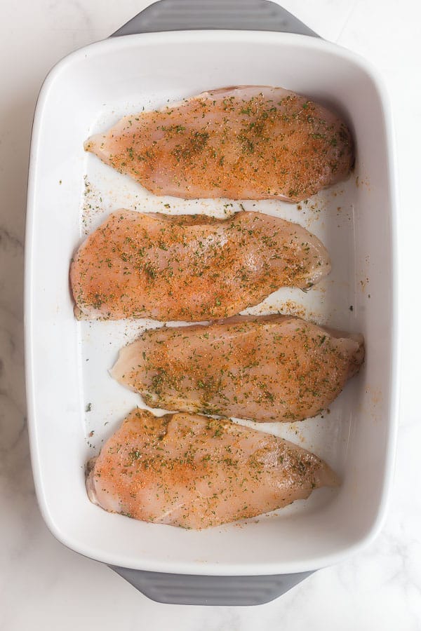 uncooked chicken breasts in baking dish with seasoning