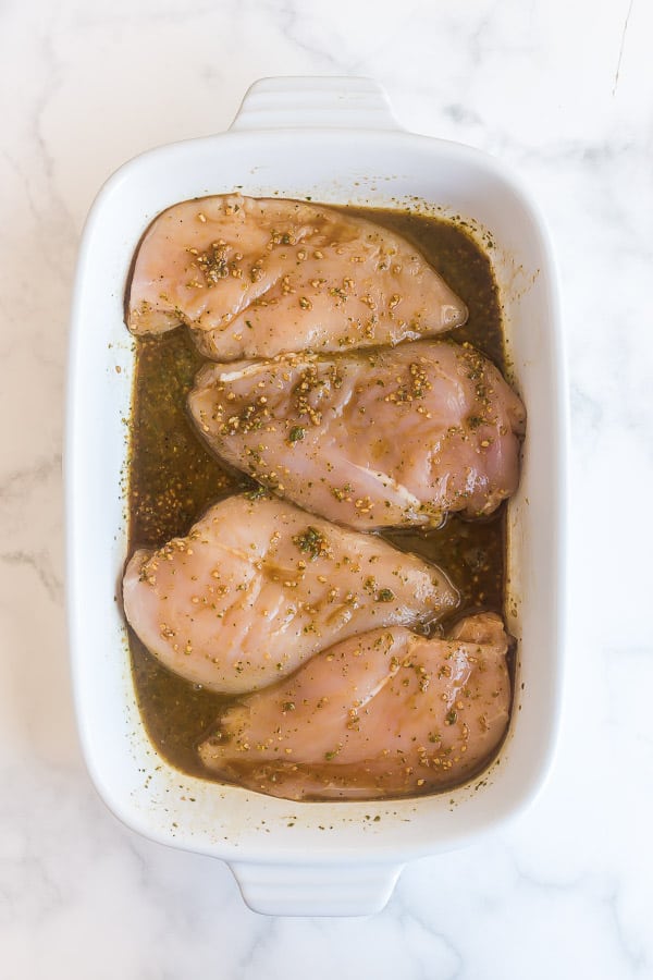 caprese marinade poured over uncooked chicken breasts in baking dish