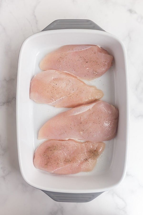 uncooked chicken breasts in baking dish with salt and pepper
