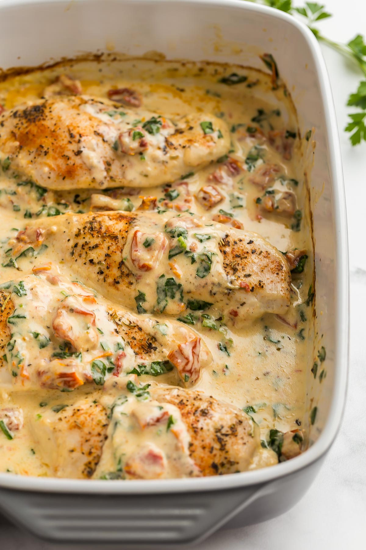 close up image of tuscan chicken in grey baking dish.