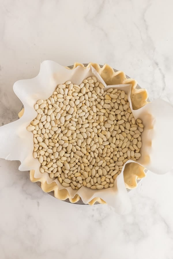 unbaked pie crust with parchment paper and pie weights for blind baking