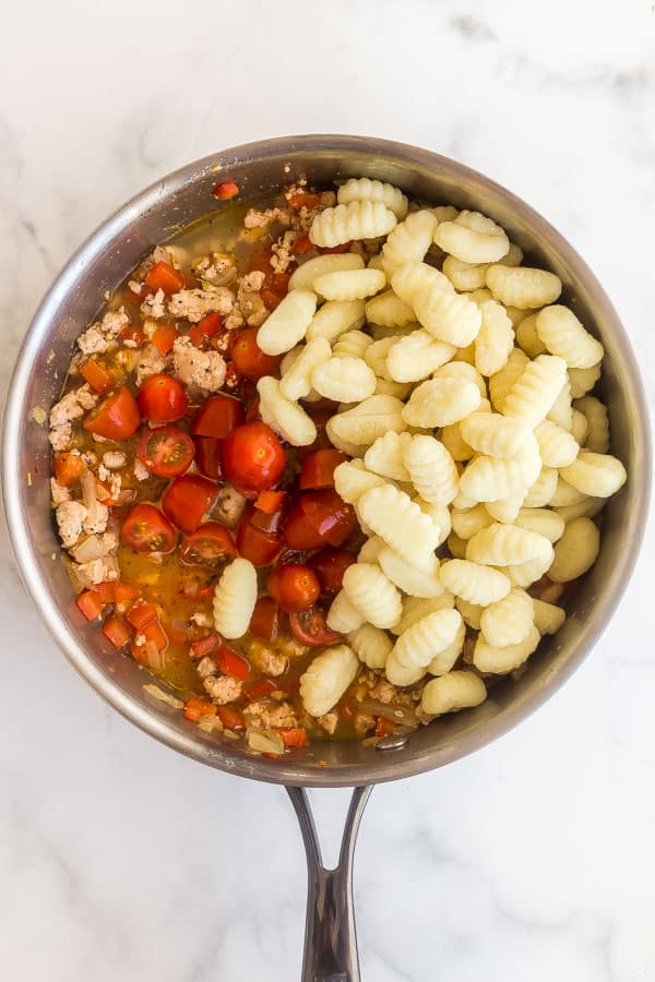 uncooked gnocchi and tomatoes added to the stainless steel pan