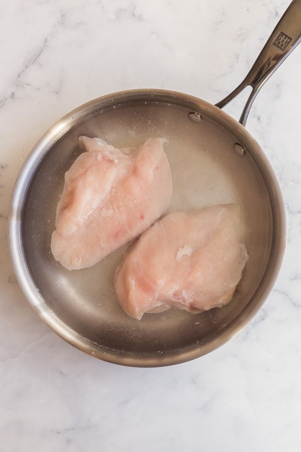 overhead image of water covering chicken breasts in pan
