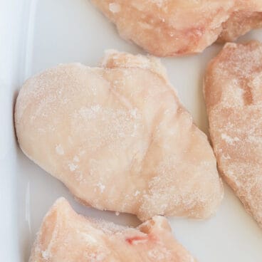 close up image of frozen chicken breasts in baking dish