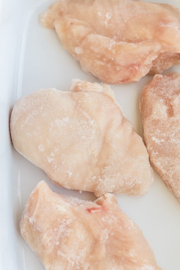 close up image of frozen chicken breasts in baking dish