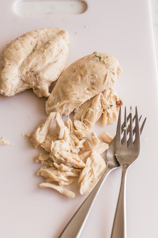 poached chicken breasts being shredded on cutting board
