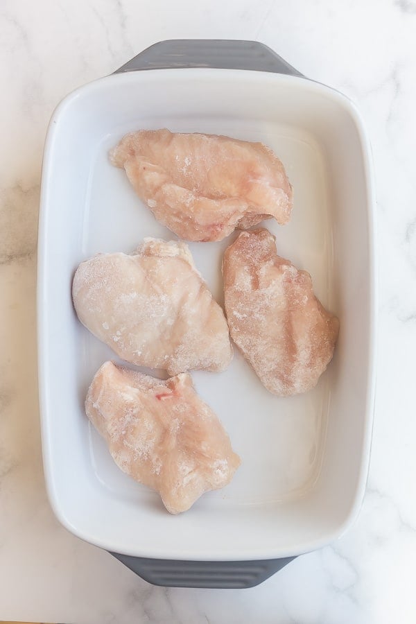 overhead image of four frozen chicken breasts in white baking dish