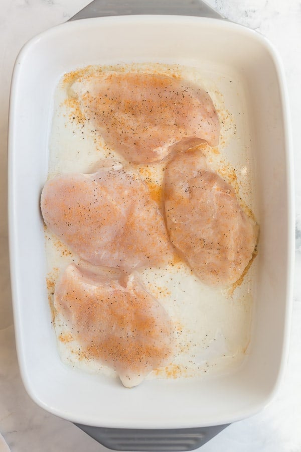 half cooked chicken breasts in baking dish with seasoning
