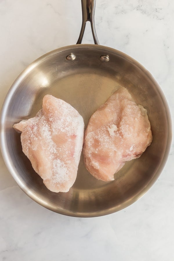 two frozen chicken breasts in stainless steel pan
