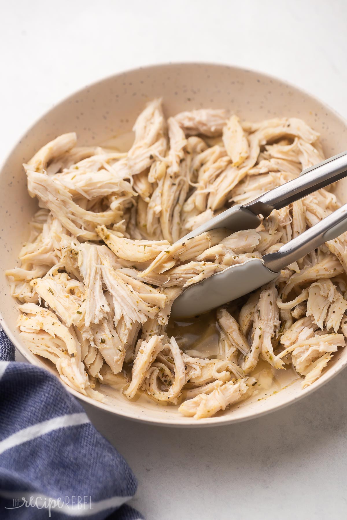 tongs picking up instant pot shredded chicken from bowl.