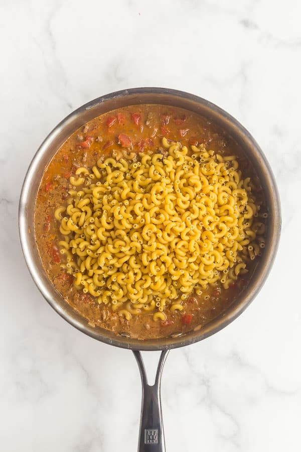 dry macaroni being added to skillet for taco mac