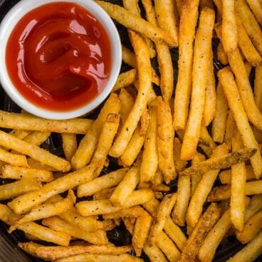 frozen french fries in air fryer with small bowl of ketchup.