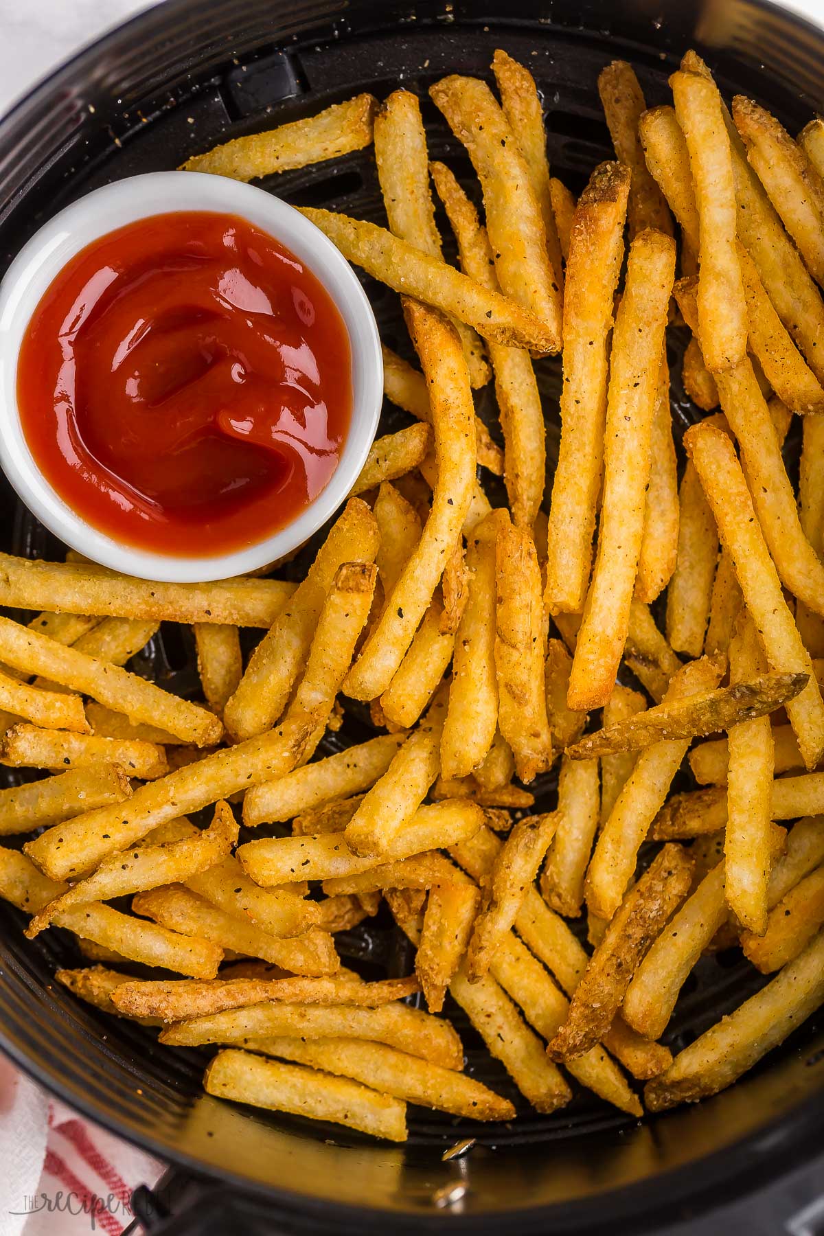 frozen french fries in air fryer with small bowl of ketchup.