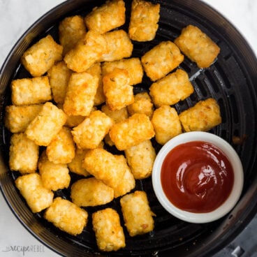 cooked tater tots in air fryer with bowl of ketchup