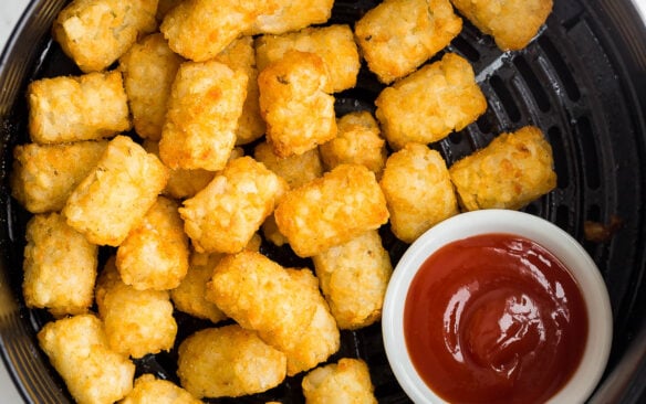 cooked tater tots in air fryer with bowl of ketchup