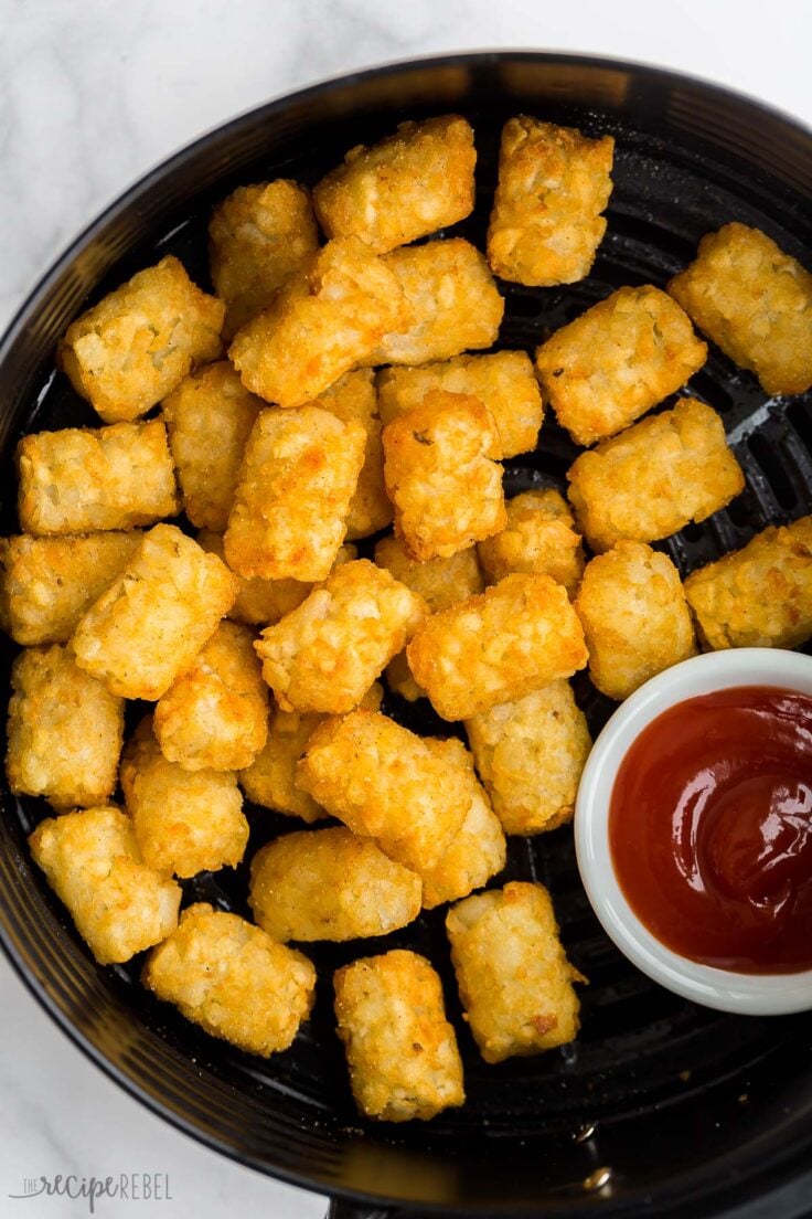 close up image of tater tots in air fryer with ketchup