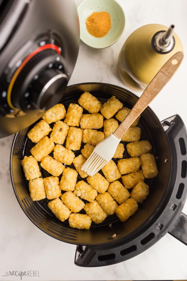 frozen tater tots in air fryer being brushed with oil