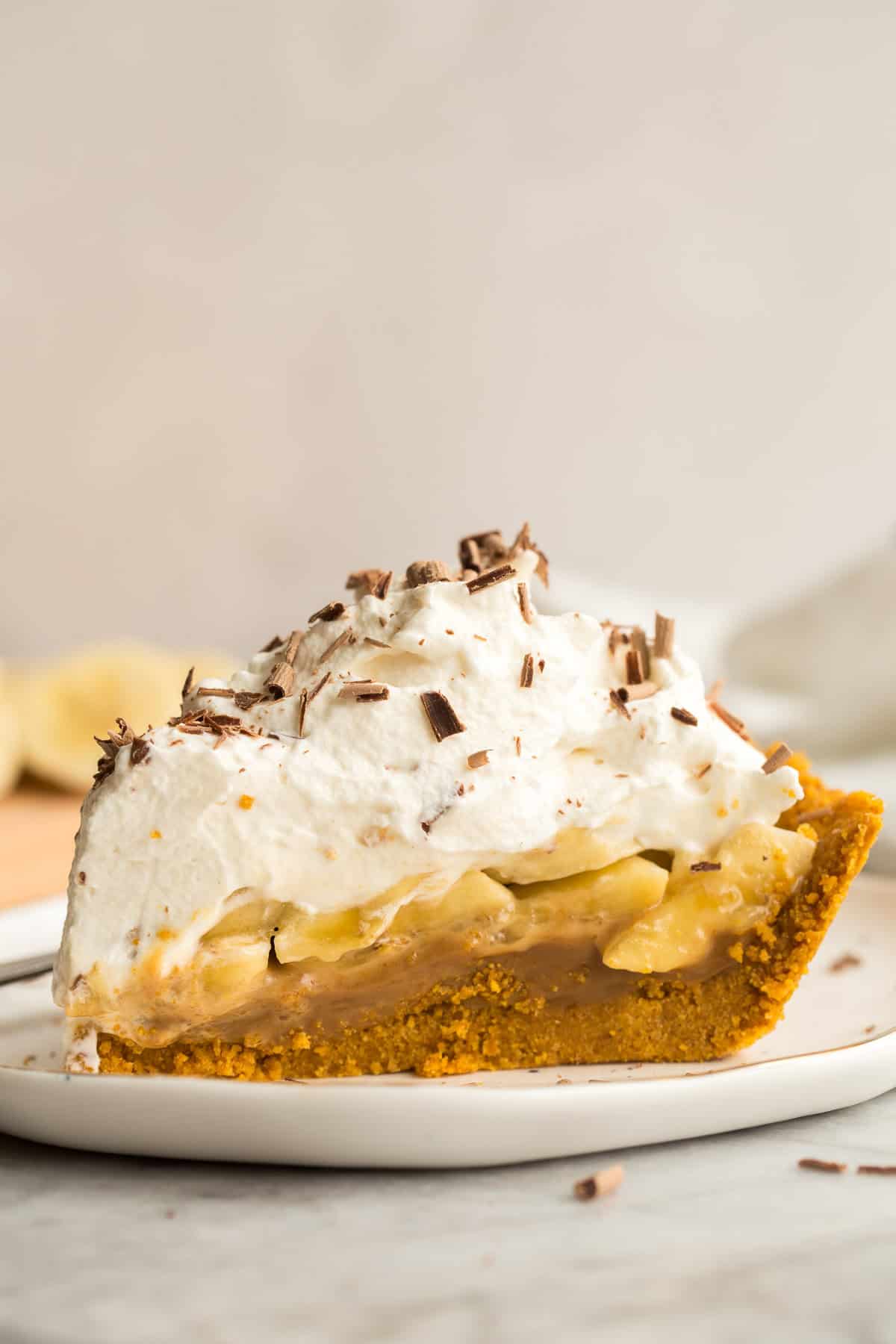 This Banoffee Pie is made with a no bake graham cracker crust, sliced bananas, dulce de leche or thick caramel, and a generous layer of sweet whipped cream! It's totally no bake and totally delicious! #pie #banana #dessert #recipes | banana recipes | no bake dessert | caramel | pie recipe | easter pie | easter desserts | banana desserts one piece of banoffee pie with whipped cream on a white plate.