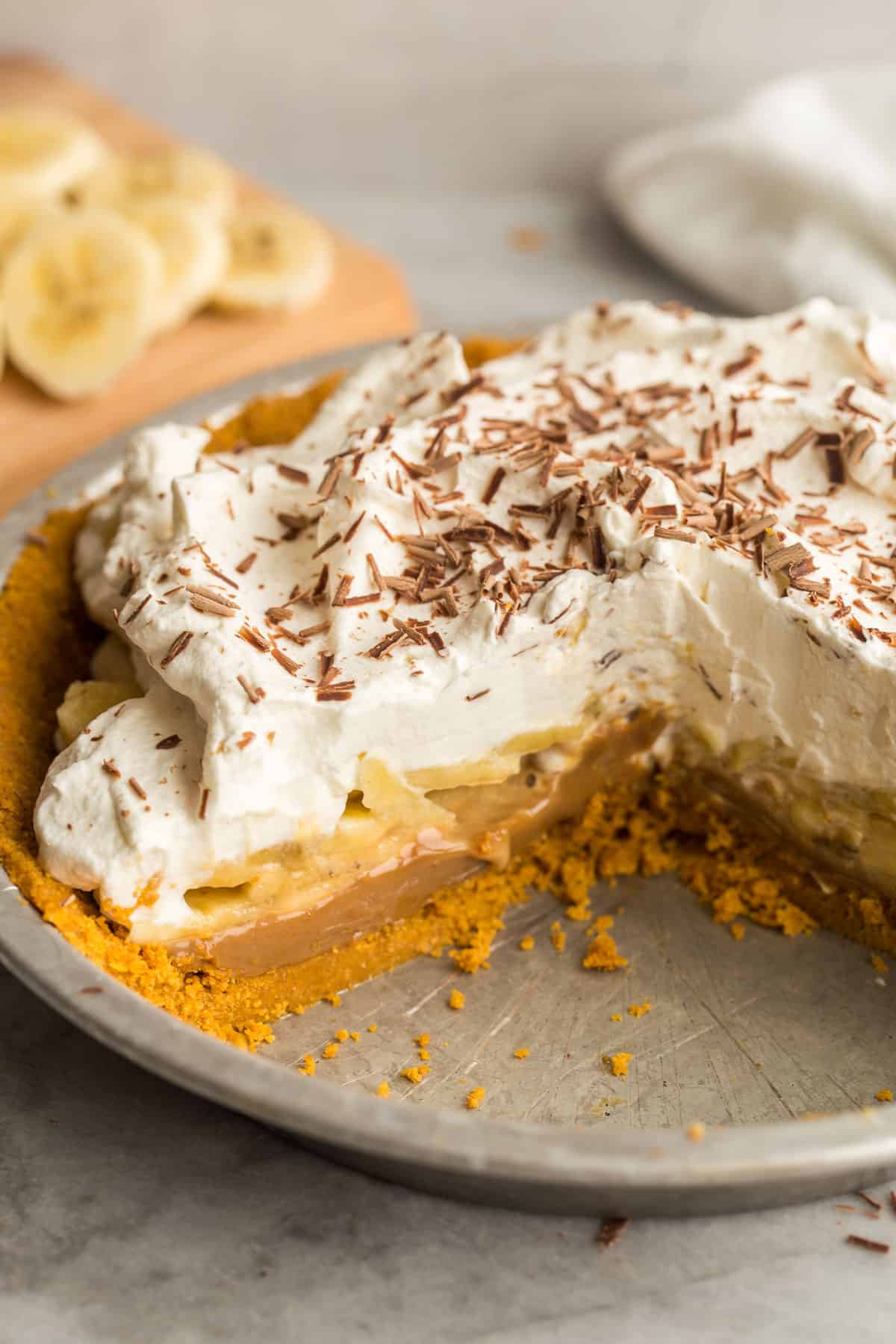 This Banoffee Pie is made with a no bake graham cracker crust, sliced bananas, dulce de leche or thick caramel, and a generous layer of sweet whipped cream! It's totally no bake and totally delicious! #pie #banana #dessert #recipes | banana recipes | no bake dessert | caramel | pie recipe | easter pie | easter desserts | banana desserts close up image of banoffee pie in tin pie plate with pieces cut out.