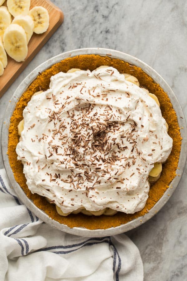 This Banoffee Pie is made with a no bake graham cracker crust, sliced bananas, dulce de leche or thick caramel, and a generous layer of sweet whipped cream! It's totally no bake and totally delicious! #pie #banana #dessert #recipes | banana recipes | no bake dessert | caramel | pie recipe overhead image of banoffee pie on marble background